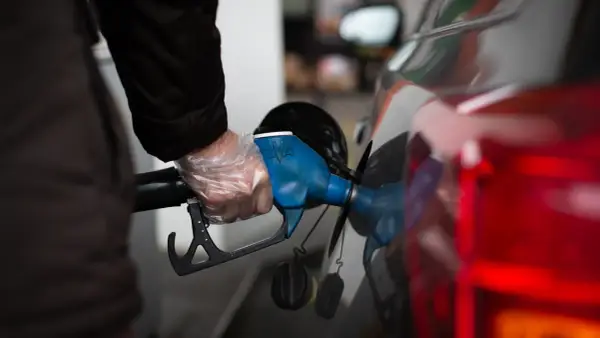 Persona con guantes pone boquilla de surtidor en coche. Un dispositivo para disminuir consumo de gasolina.