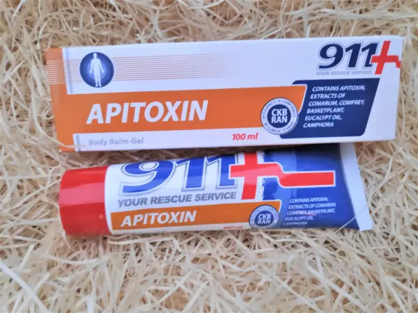 Dwa opakowania kremu z jadem pszczelim "Apitoxin" 911+ na tle słomy.