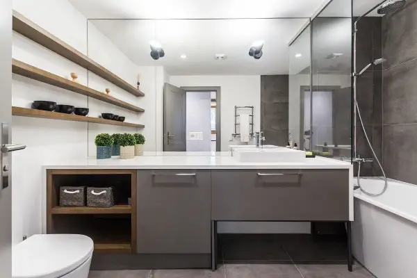 Moderno baño con ducha, bañera y lavabo sobre mueble gris. Estanterías de madera con cuencos negros. Un ejemplo de presupuesto de reforma de baño.