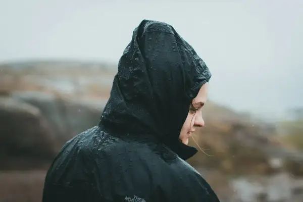 Person i regnkläder med huvan uppdragen, droppar på tyget. Vattenpelare 10000 klarar detta väder.