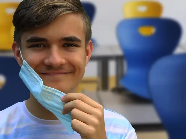 Joven sonriente se quita mascarilla, recordando la importancia de conocer los **covid en niños sintomas** para su bienestar.