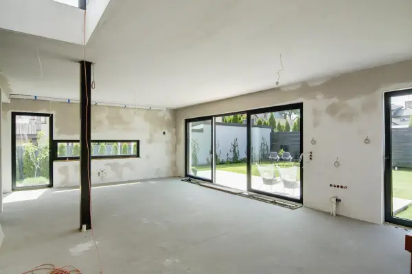 Wnętrze domu w budowie, przygotowane do tynkowania. Duże okna wychodzą na ogród. Szacowany koszt tynkowania domu 120m2.