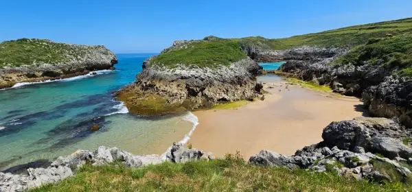 Una cala asturiana con aguas turquesas y arena dorada, rodeada de acantilados verdes. Un paraíso entre las playas más bonitas de Asturias.
