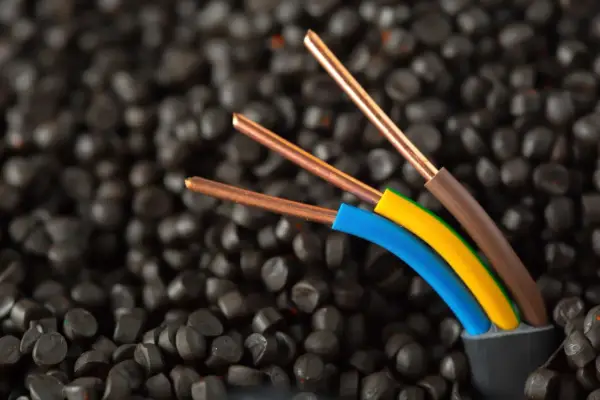 Trois fils électriques aux conducteurs en cuivre, dont un fil marron électrique, sortent d'un câble noir sur un fond de granulés noirs.