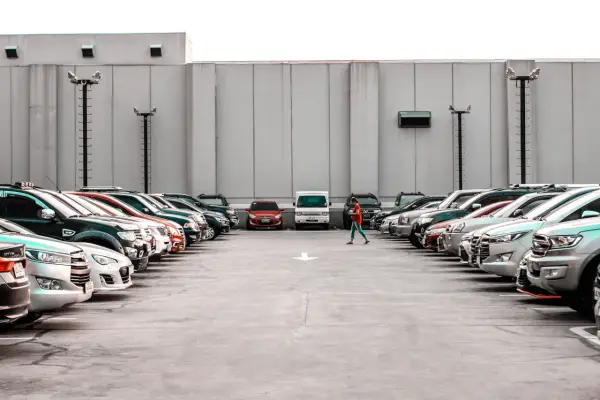 Rząd samochodów na parkingu, jedna osoba idzie pośrodku.