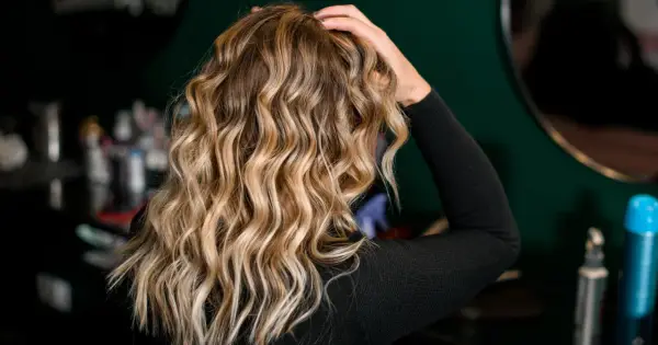 Blond włosy z falami, ułożone z pomocą aktywatora skrętu. W tle kosmetyki fryzjerskie.