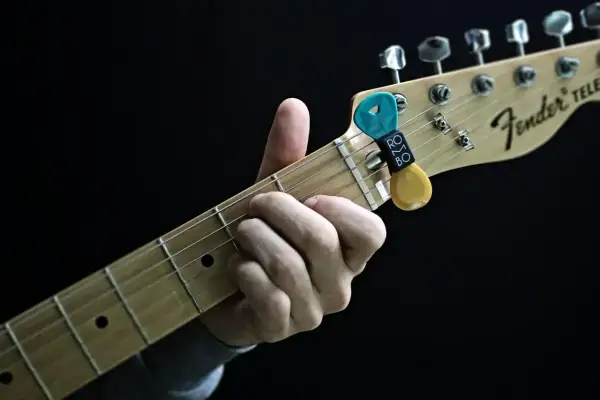 Dłoń grająca akord na gryfie gitary Fender Telecaster. Kostka z uchwytem na gryfie.