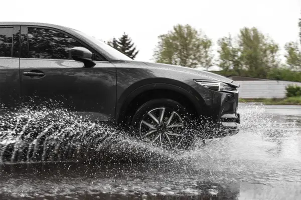 Ciemny samochód na mokrej drodze, koło rozpryskuje wodę, groźny aquaplaning.