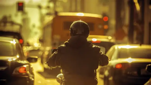 Motocyklista w kasku i kurtce w korku miejskim. Czy motor może jechać między samochodami? Tak, ten motocyklista próbuje.
