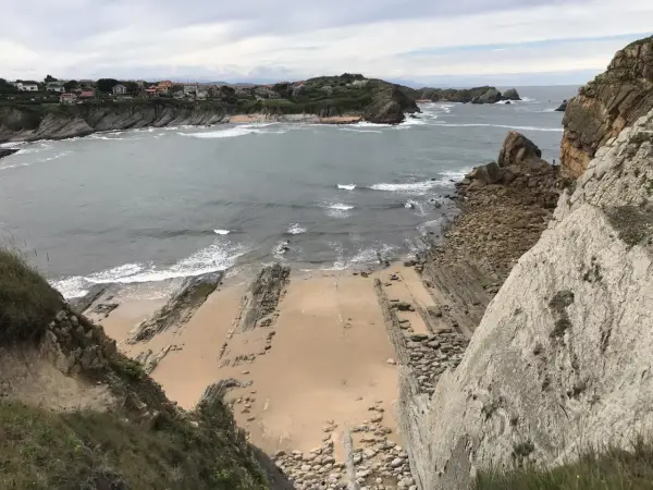 Vista panorámica de la playa San Juan de la Canal, con formaciones rocosas y casas en la costa.