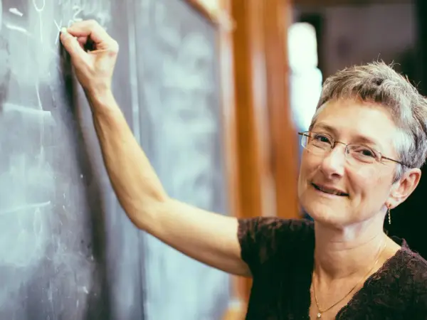 Lehrerin schreibt an Tafel. Was verdient ein Gymnasiallehrer? Sie lächelt wissend.