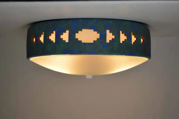 Lámpara techo azul turquesa con diseño geométrico calado, emite una luz cálida y acogedora.