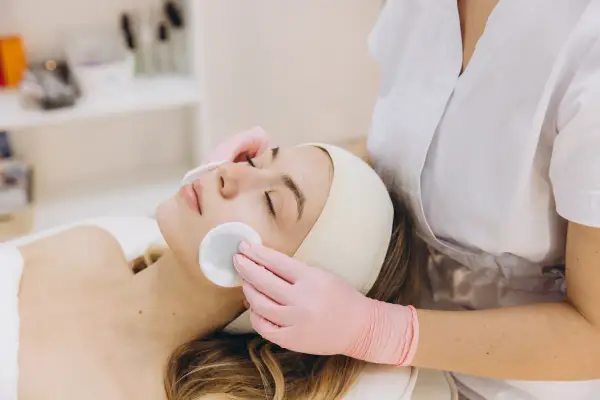 Una donna riceve una pulizia del viso con dischetti di cotone. La durata di una pulizia del viso varia, ma questo momento di relax è prezioso.