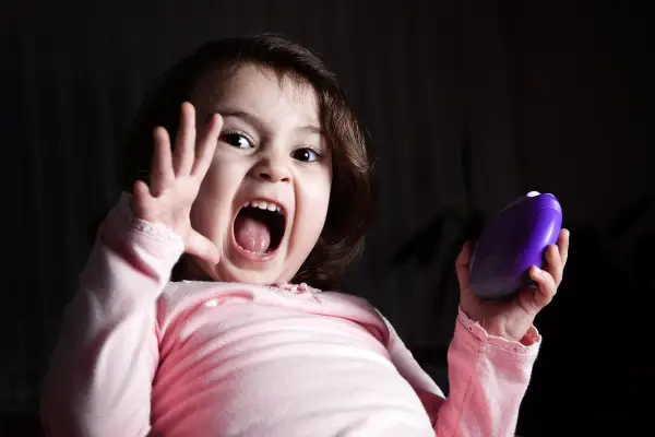 Niña con expresión de miedo, gritando y levantando una mano. Sostiene un objeto morado. Representa el miedo en niños de 6 a 12 años.