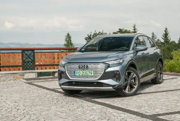 Szary Audi Q4 na kamienistym podjeździe, z widokiem na góry i las.