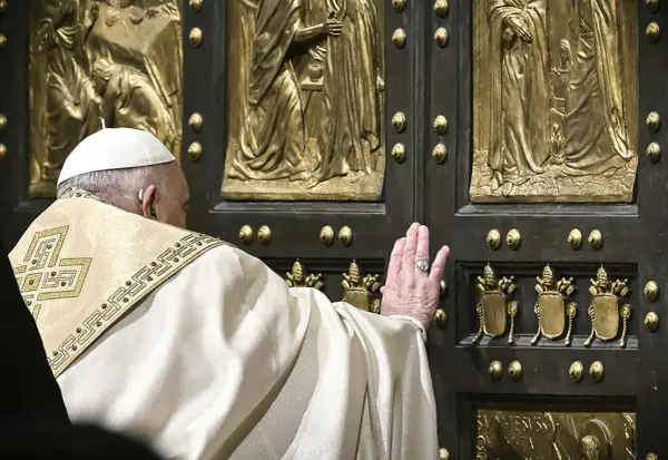 Papst Franziskus berührt die heilige Pforte des Petersdoms. Die bronzene Tür ist mit Reliefs verziert, die biblische Szenen darstellen.