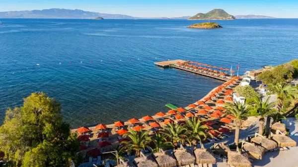 Piękna plaża z rzędem pomarańczowych parasoli i leżaków, drewniany pomost, palmy i turkusowe morze. Idealne miejsce na wakacje, zgodnie z kadikale resort opinie.
