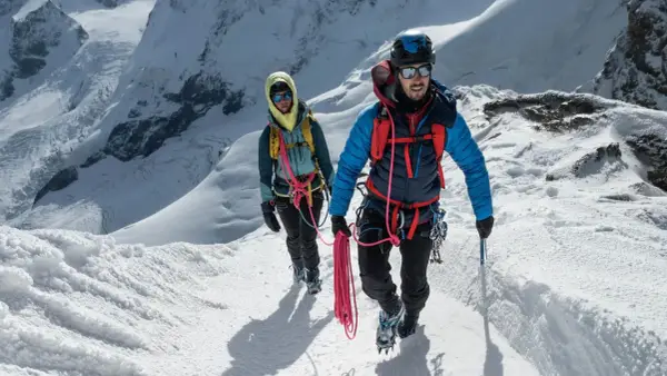 Dwóch alpinistów wspinających się po ośnieżonym zboczu, z liną i sprzętem. Zapewniają sobie asekurację lotną w trudnym terenie.