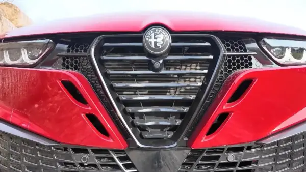 Czerwona Alfa Romeo z bliska. Widoczny grill w kształcie tarczy z logo, reflektory i detale karoserii w zbliżeniu. Alfa makro.