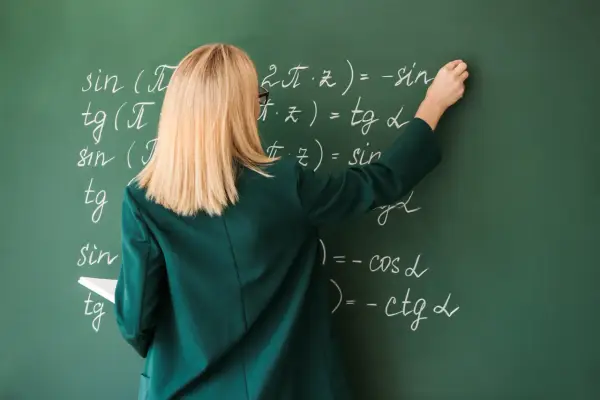 Nauczycielka pisze kredą wzory matematyczne na zielonej tablicy.