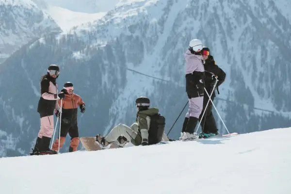 Grupa narciarzy i snowboardzistów odpoczywa na stoku, podziwiając majestatyczne góry Sierra Nevada.
