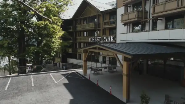 Elegancki hotel 5 gwiazdkowy Forest Park otoczony zielenią, z parkingiem i zadaszonym wejściem.