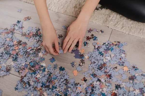 Ręce układają puzzle na podłodze. Po skończeniu dowiesz się, jak powiesić puzzle na ścianie.