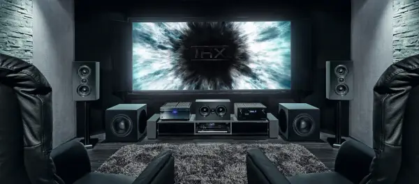 Installation home cinema avec écran THX, amplificateur, enceintes et fauteuils en cuir noir pour une expérience immersive.