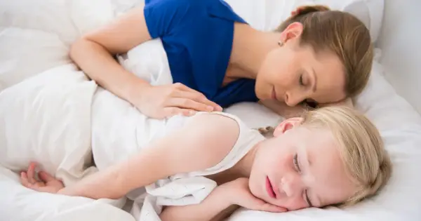 Mama i dziecko śpią razem, otuleni białymi pościelami. Czy dzieci powinny spać z rodzicami? Ta chwila spokoju sugeruje, że tak.