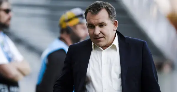 Żyżyński dziennikarz sportowy w garniturze, z uwagą obserwuje wydarzenia na boisku.