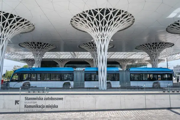 Nowoczesny dworzec autobusowy w Lublinie z niebieskim autobusem. Architektura przypomina drzewa, jakby podróż z Torunia do Lublina była podróżą przez futurystyczny las.