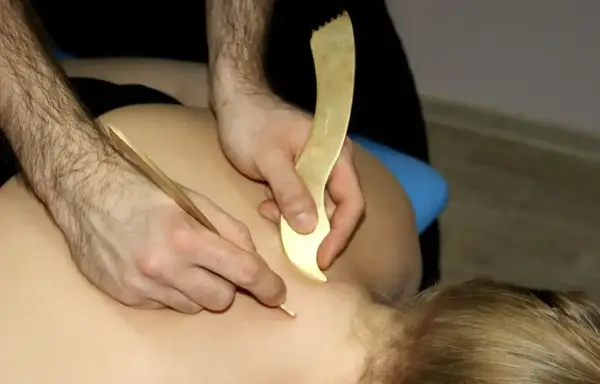 Masaż narzędziami do pinoterapii. Terapeuta pracuje nad karkiem pacjenta, używając złotych przyrządów do głębokiego masażu tkanek.