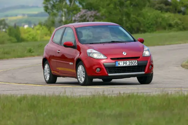 Czerwony Clio 3 na zakręcie drogi, otoczony zielenią.