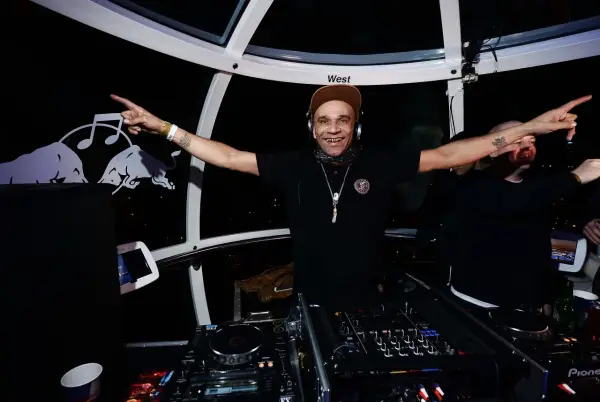 Un dj rap souriant, casqué, bras écartés, anime la soirée dans une cabine panoramique.