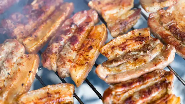Kawałki soczystego boczku surowego pieką się na grillu, otoczone dymem.