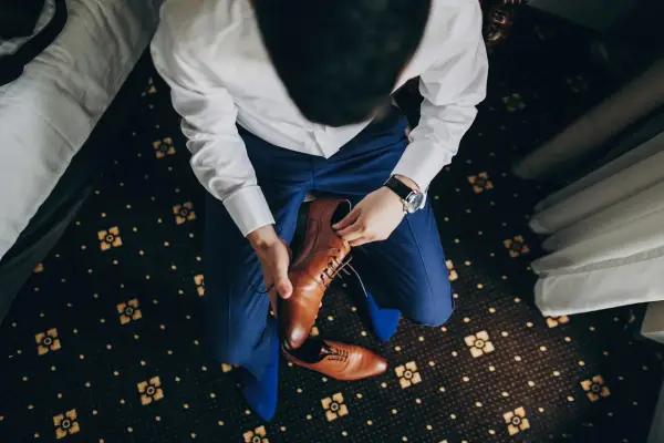 Mężczyzna w niebieskim garniturze i białej koszuli zakłada brązowe, eleganckie buty. Idealne pytanie: jakie buty do niebieskiego garnituru?
