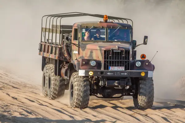 Kraz 255 z załogą przemierza piaszczysty teren, wzbijając tumany kurzu.