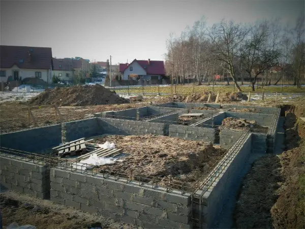 Budowa fundamentów domu w trakcie. Widać zbrojenie i bloczki betonowe, przygotowywane pod izolację poziomą fundamentów.