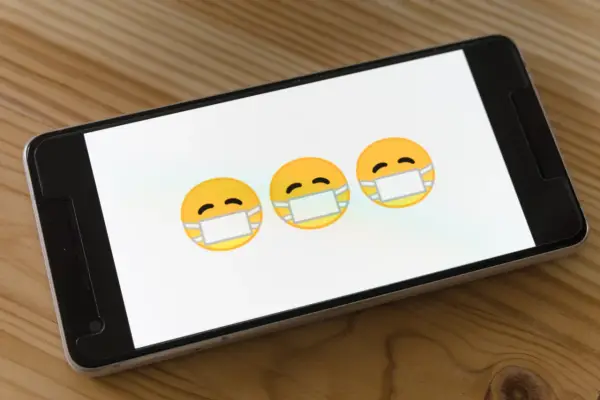 Trzy emoji w maseczkach na ekranie smartfona. Dowiedz się, jak usunąć wirusy z iPhone.