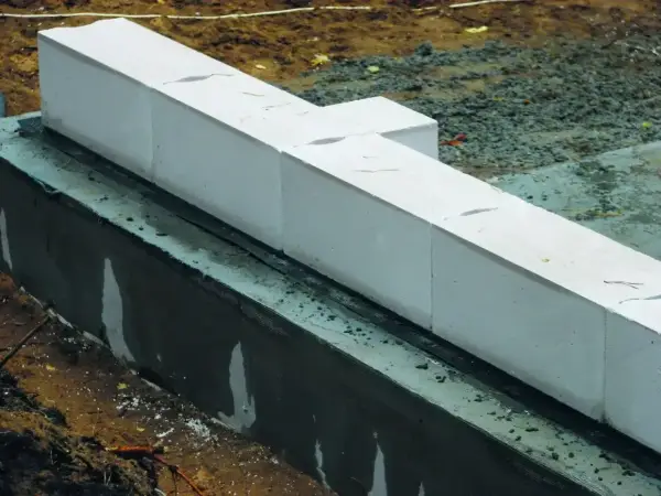 Białe bloczki z betonu komórkowego, prawdopodobnie do budowy fundamentów, leżą na warstwie izolacji. Nivoplan zapewnia stabilność konstrukcji.