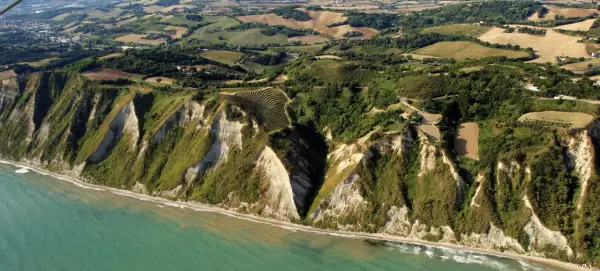 Scogliere a picco sul mare turchese a Gabicce Mare, Marche. Campi coltivati e vegetazione rigogliosa adornano le colline retrostanti.