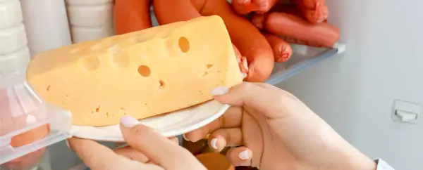 Una mano prende un pezzo di formaggio svizzero dal frigorifero, accanto a delle salsicce.