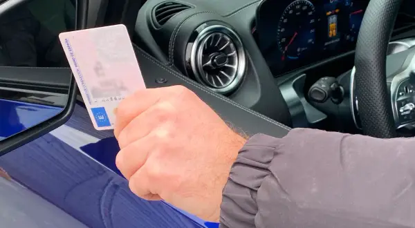 Mano sujetando permiso de conducir español dentro de un coche moderno, anticipando la conducción autónoma en España.