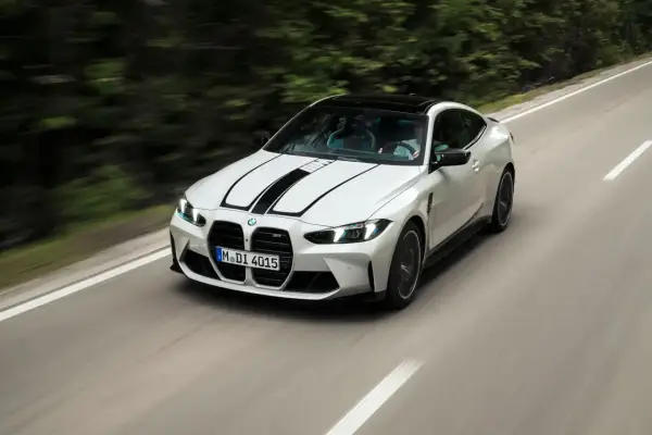 Białe BMW F82 z czarnymi pasami na masce pędzi po krętej drodze wśród zieleni.