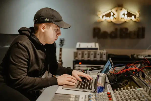 Un jeune beatmaker français concentré sur son ordinateur portable dans un studio d'enregistrement, une canette Red Bull à portée de main.