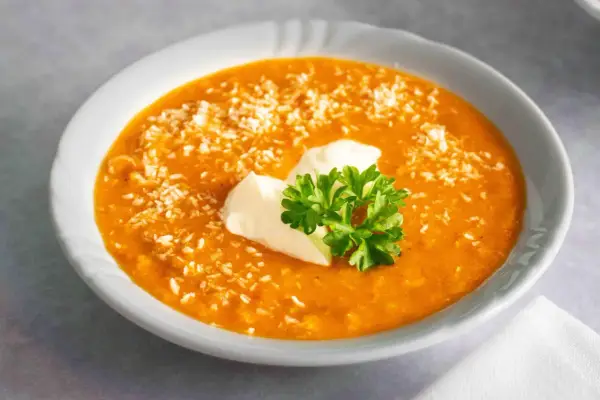 Ein cremiger, orangefarbener rote linsen eintopf, bestreut mit Kokosraspeln und garniert mit einem Klecks Sauerrahm und frischer Petersilie.