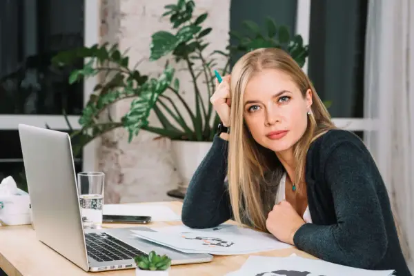 Blondynka z zielonym długopisem w dłoni, zastanawia się nad różnymi rodzajami odpoczynku, siedząc przy biurku z laptopem.