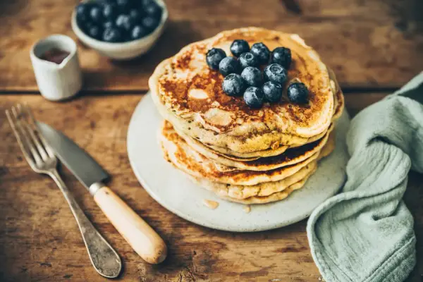 Pile de pancakes au levain garnis de myrtilles, sur une assiette, avec une fourchette et un couteau.
