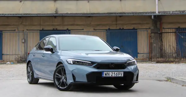 Nowy Honda Civic 11. generacji w szarym kolorze prezentuje się elegancko na tle industrialnego krajobrazu.