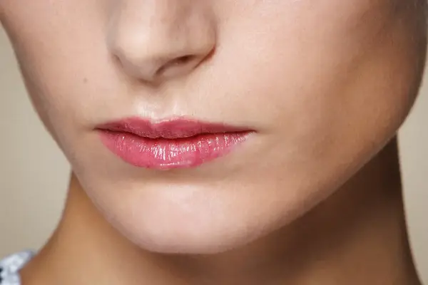 Labbra sottili e lucide con un tocco di gloss rosa, che catturano la luce.